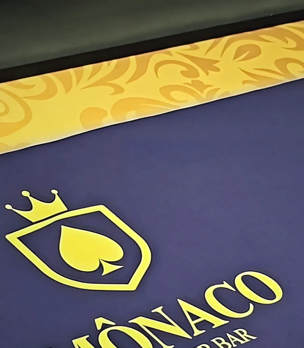 O feltro índigo de uma mesa do Monaco, com o trilho de arabesco dourado e o escudo da casa