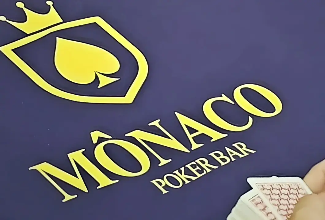 O feltro azul de uma mesa do Monaco, com o escudo e o nome da casa em amarelo, e as cartas na mão de quem joga