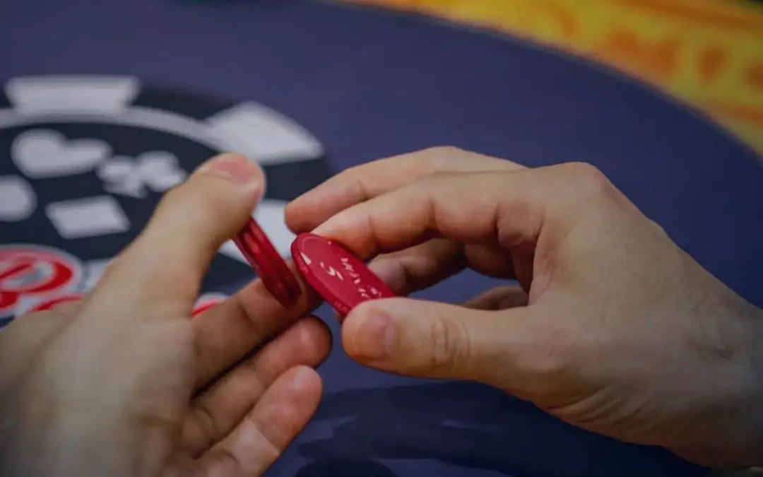 Mãos de um jogador separando fichas vermelhas sobre o feltro azul de uma mesa do Monaco